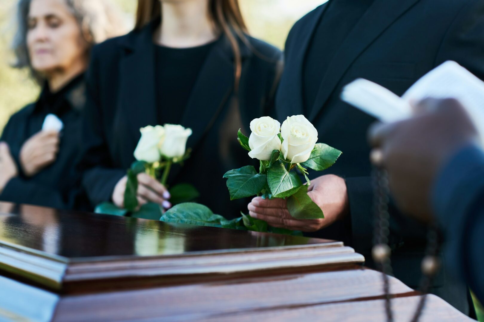 Focus on two fresh white roses held by man in black suit during funeral service